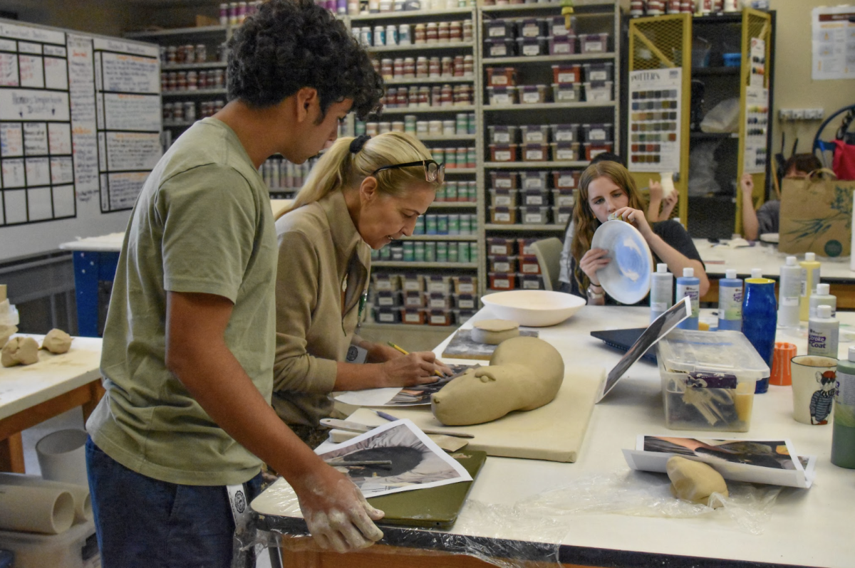 While junior Sophia Cubbage puts finishing touches on her piece, senior Niko Torres Holloway gets some assistance from ceramic teacher Ms. Luiza Grandchamp. The classroom is filled with the sound of the wheel spinning, the scrape of tools on clay and students chatting as they work. “Ceramics is a process, and it's about learning how to deal with mistakes. I'm here to help guide them, but it is their creativity that shapes each piece,” Ms. Grandchamp said.